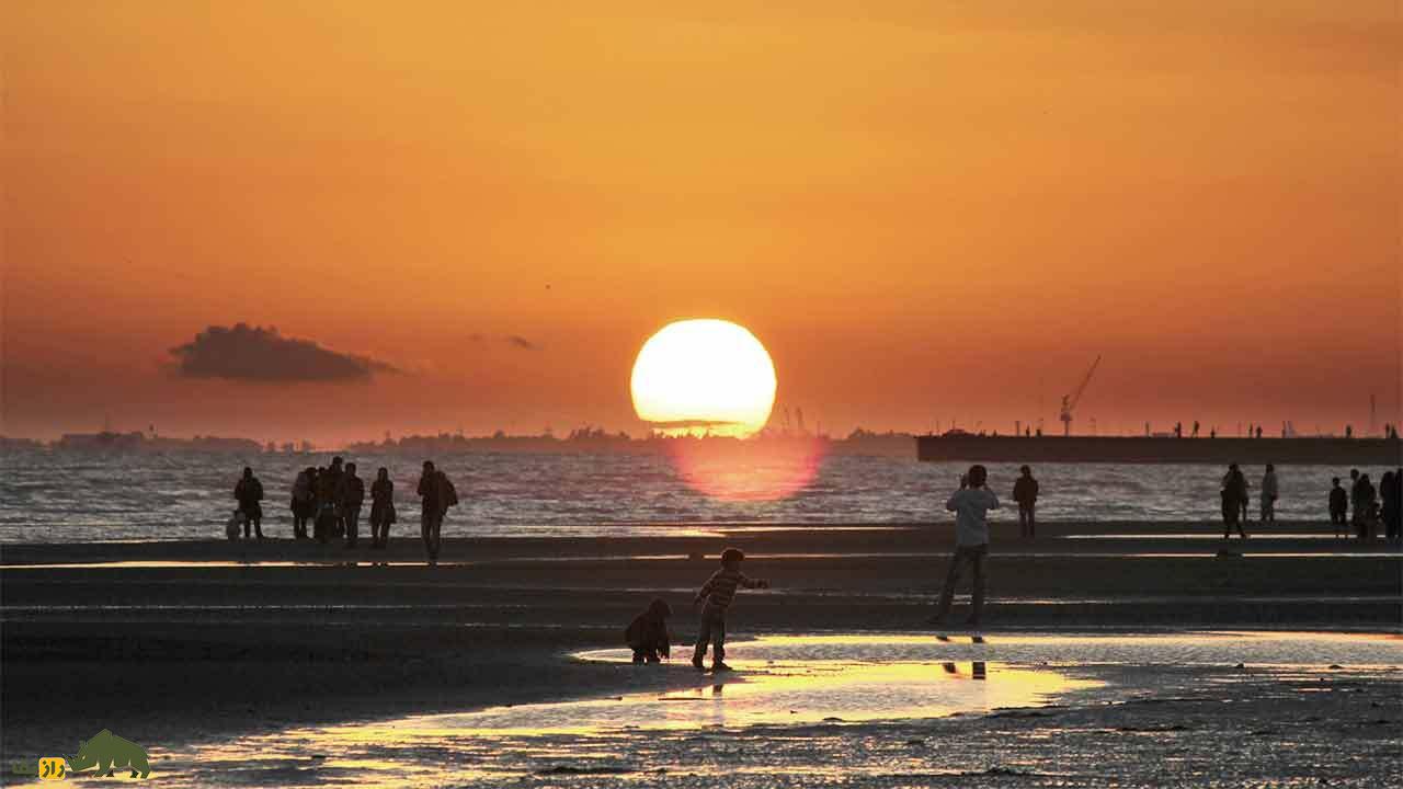 مردم لب ساحل هنگام غروب خورشید در خلیج فارس